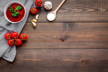 Homemade tomato ketchup with cherry tomatoes, garlic and basil on dark wooden background top view space for text