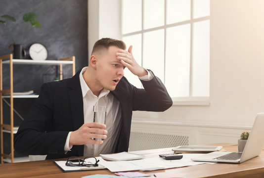Stressed male manager working on laptop and drinking water