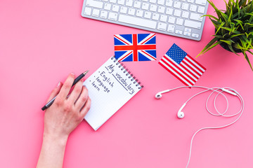 Learn new english vocabulary. Learn landuage concept. Computer keyboard, british and american flags, notebook for writing new vocabulary on pink background top view