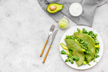 Spinach pancakes with spinach leaves and avocado slices on plate on grey background top view copy space