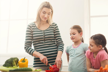 Beautiful woman with her daughters cooking salad