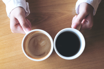 Top view image of hands holding two white cups of coffee on wooden table in cafe