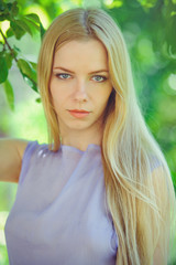 Attractive modest young girl with blond dren hair and natural make-up in purple dress outdoors, tenderness and softness on nature background