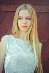 Fototapeta premium Attractive modest young blond woman on red wooden background her hair painted in pink striped striped, in blue dress shy and inquisitive
