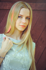 Fototapeta premium Attractive modest young blond woman on red wooden background her hair painted in pink striped striped, in blue dress shy and inquisitive
