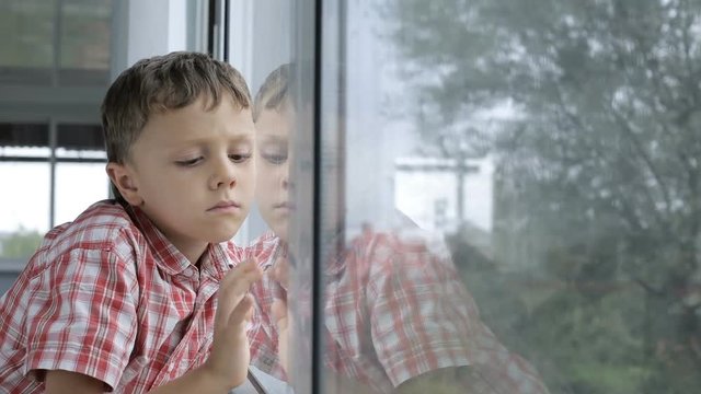 sad little boy standing near a window at home  at the day time