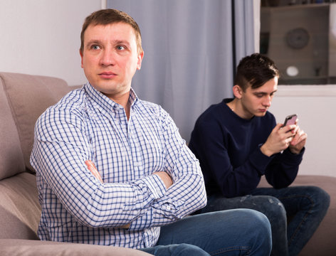 Man with his adult son are conflicting and boy playing with phone
