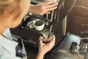 Experienced barista steaming milk in professional coffee machine