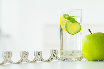 Green apples, glass water with mint leaves, lemon and cucumber, tape measure - concept of healthy eating and modern lifestyle