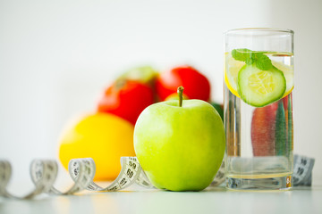 Green apples, glass water with mint leaves, lemon and cucumber, tape measure - concept of healthy eating and modern lifestyle