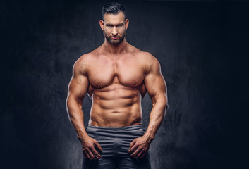 Fototapeta premium Portrait of a shirtless tall huge male with a muscular body with a stylish haircut and beard, in a sports shorts, posing in a studio.