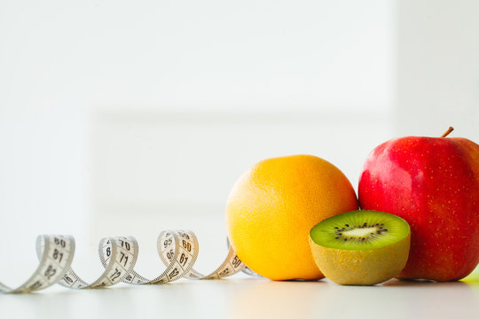 Orange, kiwi and apple surrounded by a tape measure on white background