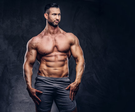 Portrait of a shirtless tall huge male with a muscular body with a stylish haircut and beard, in a sports shorts, posing in a studio.