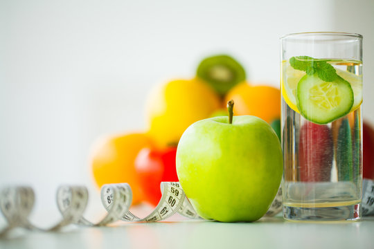 Green apples, glass water with mint leaves, lemon and cucumber, tape measure - concept of healthy eating and modern lifestyle