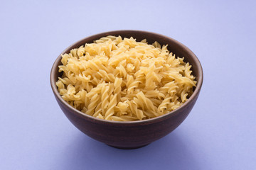 Spiral pasta in bowl on purple background