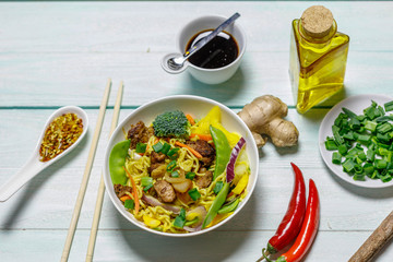 Chinese noodles with vegetables, mushrooms and meat in bowl on light blue wooden ruxtic table, top view © jarvna