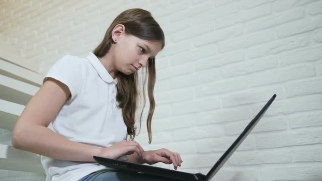 online internet pastime. young teen seeting on stairs and browsing laptop entertainment resources.
