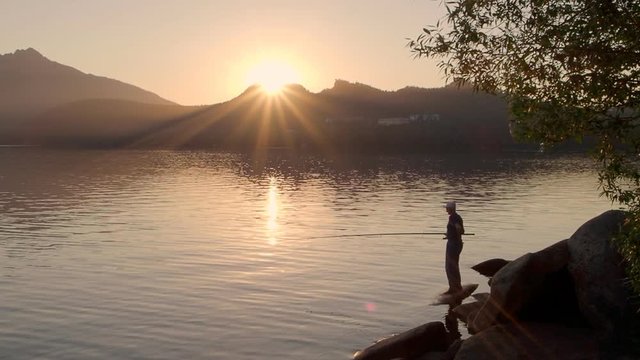 Man fishing by mountain lake at sunset in Kazakhstan