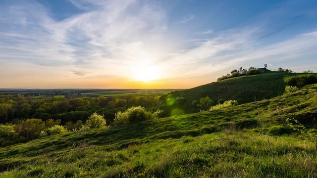 Timelapse of the sunset above meadow and agriculture land. Beautiful countryside land with sun and clouds on the sky. Spring and summer weather, colorful nature. Peoples walking on the small hill