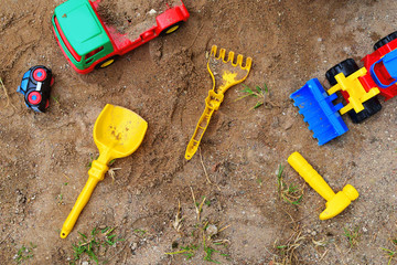 Top view of colorful plastic cars and toy tools on sand background.  Children summer activities outdoors.