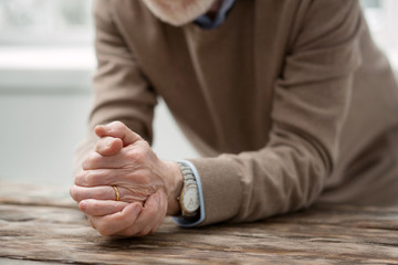 Sad feelings. Nice aged man putting his hands on the table while being all alone