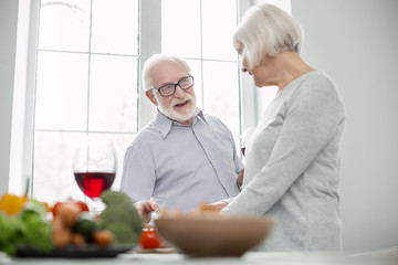 Delicious food. Pleasant nice aged couple talking to each other while cooking dinner together