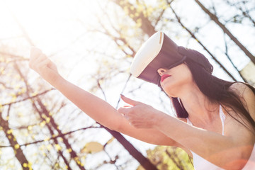 Naklejka premium Virtual reality, fun in the park. A woman relaxes in the park using googles VR. The girl imagines that she is climbing the rope. Spending free time outside, lifestyle concept.