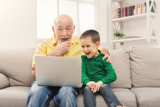 Little boy teaching his grandfather to use laptop