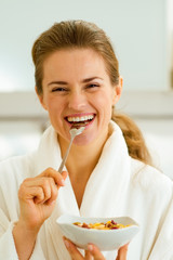 Smiling young woman in bathrobe eating healthy breakfast