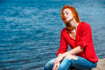 Fototapeta na wymiar Joyful redhead woman sitting comfortably, feeling serene and free and enjoying a sunny day at the beach.