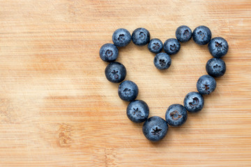 Heart symbol formed with blueberries on wooden background