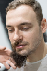 Fototapeta premium Handsome bearded man is getting shaved by hairdresser at the barbershop