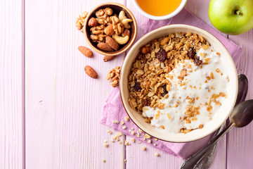 Granola with yogurt in bowl on pink wooden background.