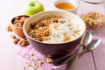 Granola with yogurt in bowl on pink wooden background.