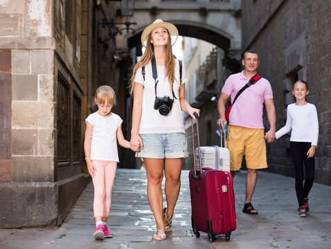 traveling family of four strolling with luggage along European city street