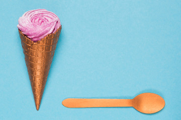 a horn with ice cream or with a cream on a blue background and one spoon, a concept