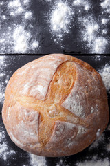Bread with flour on a black background, wheat bread from a stove on dark boards, dough for a designer, copy space, rustic style, flour on a black background, top view, cooking
