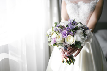 Brides wedding bouquet with peonies, freesia and other flowers in women's hands. Light and lilac...