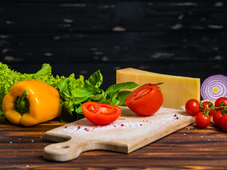 wooden board with parmesan cheese, fresh cherry tomatoes, lettuce, sea salt, paprika and yellow bulgarian pepper, red onion. Appetizing still life from vegetables