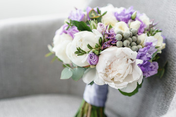 Brides wedding bouquet with peonies, freesia and other flowers on black arm chair. Light and lilac spring color. Morning in room