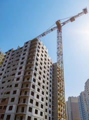 Fototapeta na wymiar Yellow crane and high building construction site against blue sky