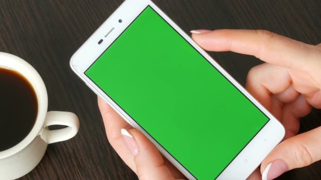 Female hands with beautiful French manicure take a white smartphone with Green Screen near white cup of coffee. Using Smartphone,Holding Smartphone with Green Screen