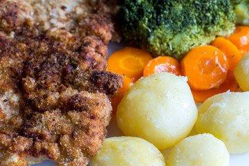 Pork cutlet with boiled vegetables, potatoes and onions. Austrian schnitzel with garnish. Top view, close up.