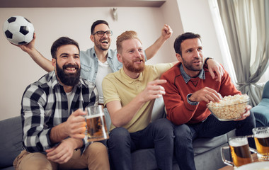Group of friends watching soccer game on television and celebrating goal.