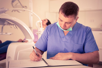 Fototapeta premium dentist in uniform writing document with visitor in dentist's office