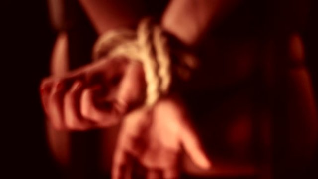girl has hands bound behind their backs with rope