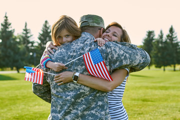 Happy soldier with his family in the sunny day. Close up hugs, reunion in the park lawn.