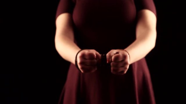 submissive woman wearing a purple dress in leather handcuffs on black background