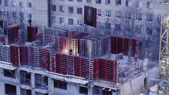 Workers on the top of the building under construction at the evening in winter. They are making formwork