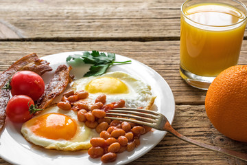 English breakfast served in a plate with fried egg, beans, tomatoes and bacon with fresh orange juice